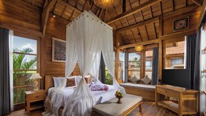 A spacious bedroom with a large bed, a wooden ceiling, and a view of palm trees. - The Kalyana Ubud Resort (Ubud)