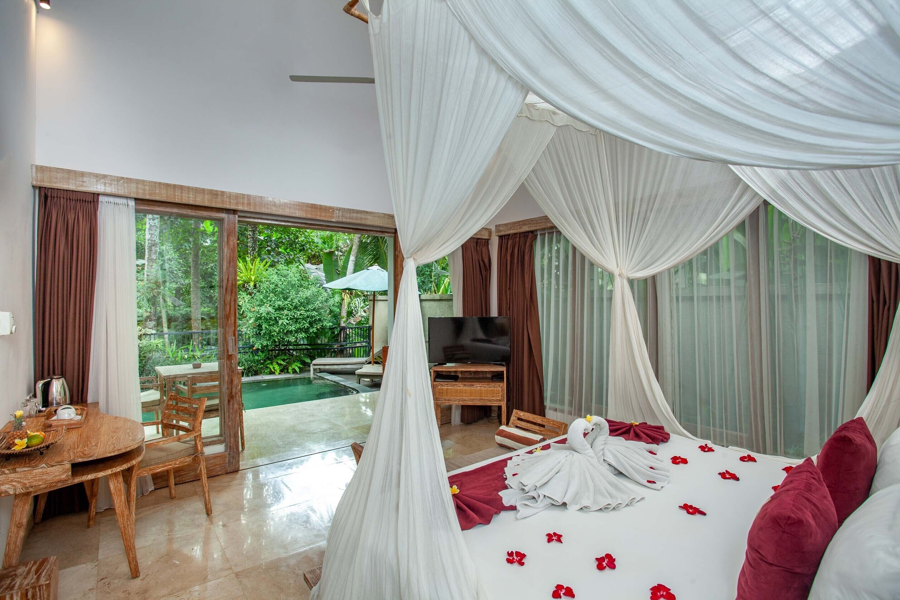 Quarto com cama, televisão, mesa de jantar e vista para piscina e vegetação.