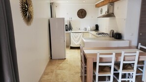 Une cuisine compacte dotée d’un îlot central, d’un réfrigérateur, d’une horloge et d’appareils électroménagers de base.