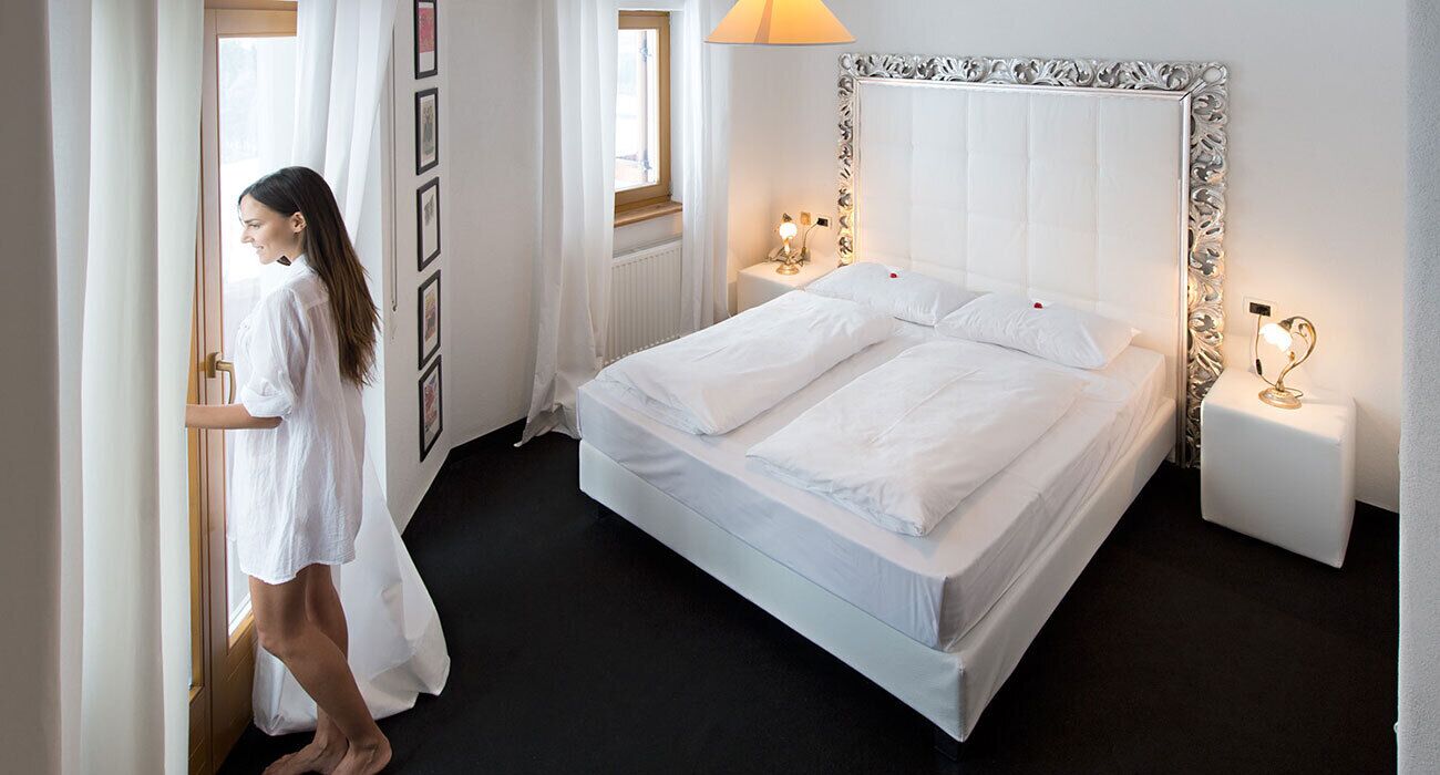 A hotel room with a large bed, white curtains, a radiator, and bedside lamps.