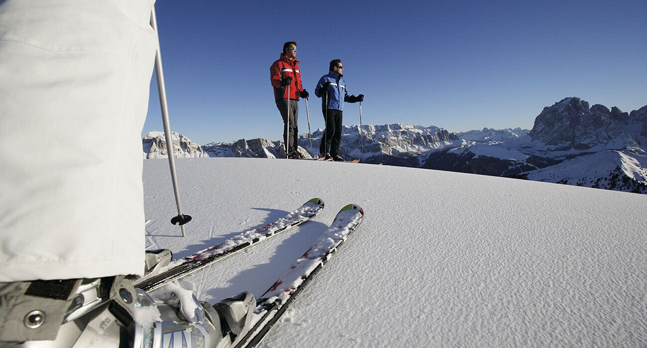 A snowy ski slope with two skiers and their skis in the foreground.