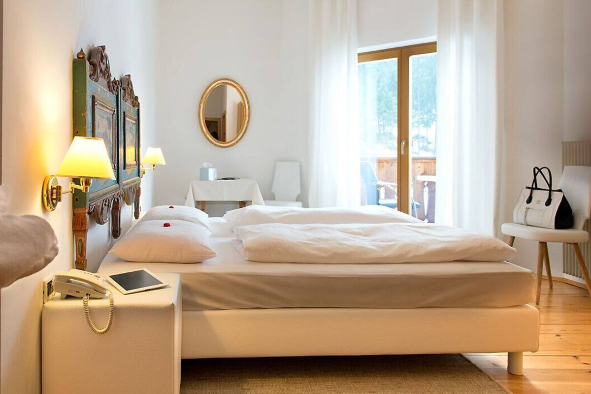 A hotel room with a bed, bedside lamps, a telephone, a chair, and a table.