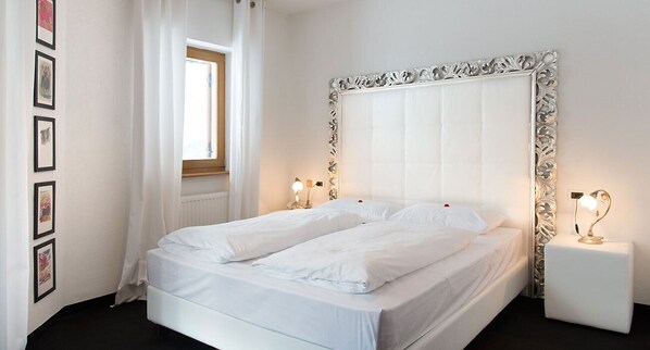 Una cama bien hecha con sábanas blancas, un cabecero decorativo, lámparas de noche y cuadros en la pared.