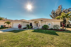 Stunning home with a beautifully manicured lawn and lush greenery, featuring a garage door, front entrance, and a charming circular window.