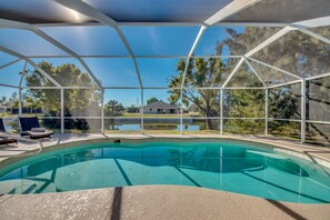 Relax by the pool surrounded by lush greenery and a tranquil body of water.