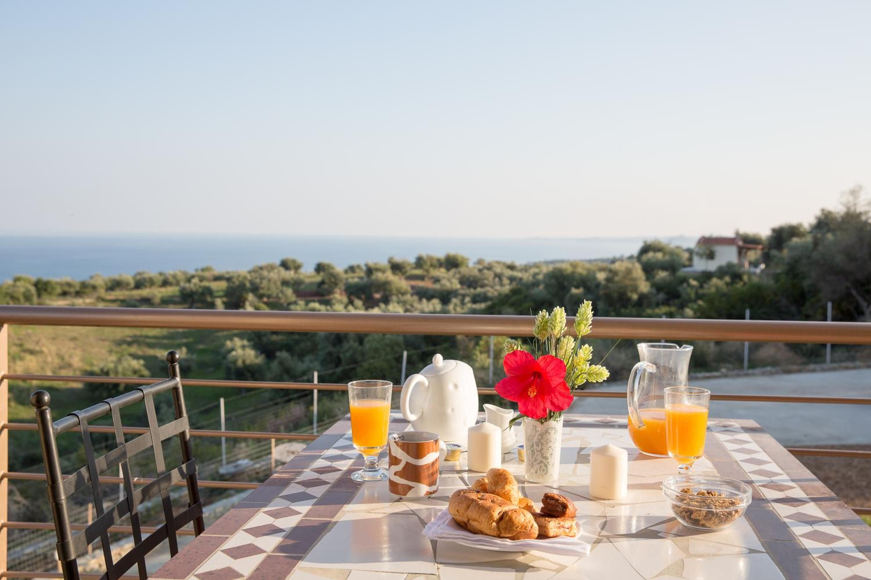 A breakfast setup on a balcony with a view of the sea and greenery.