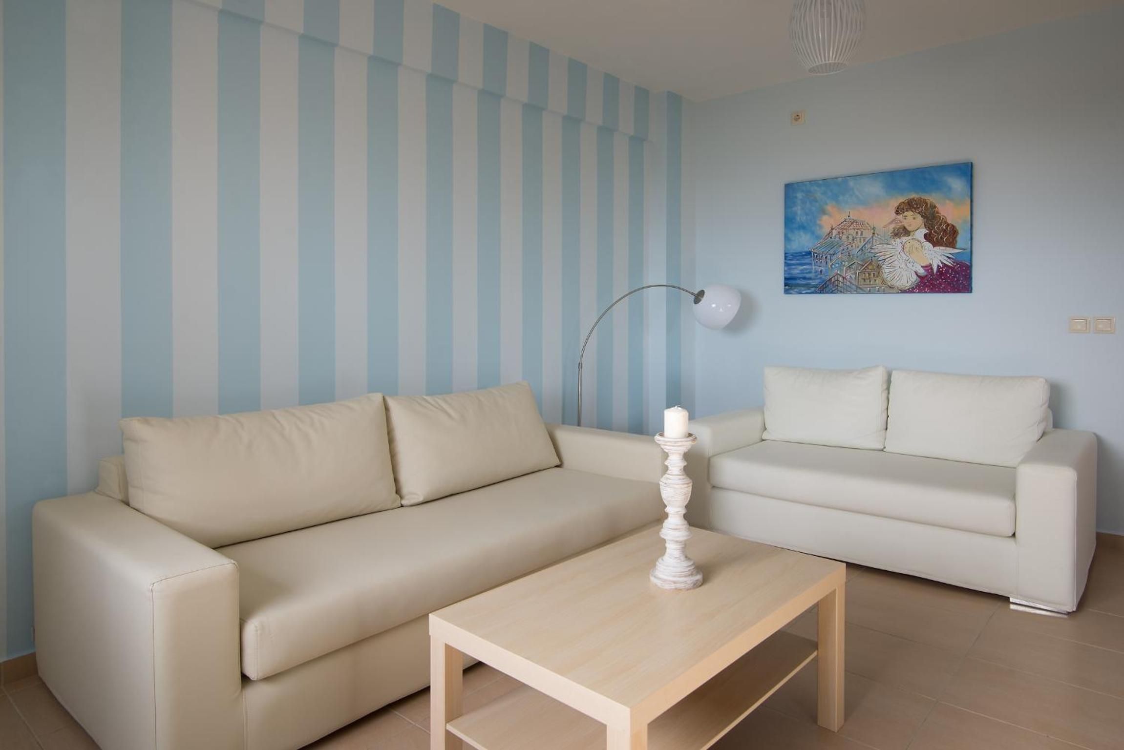 A living room with two beige sofas, a wooden coffee table, a floor lamp, and a painting on the wall.