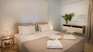 Een net opgemaakt bed met witte lakens, een bedlampje en een klein tafeltje met een telefoon en oplader.