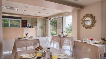 A dining area with tables set for breakfast, clear chairs, and a view of the outdoors.