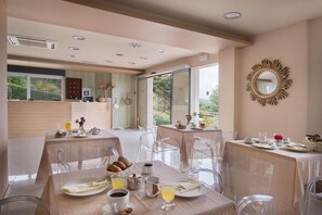 A dining area with tables set for breakfast, clear chairs, and a view of the outdoors. - Baywatch Hotel (Messini)
