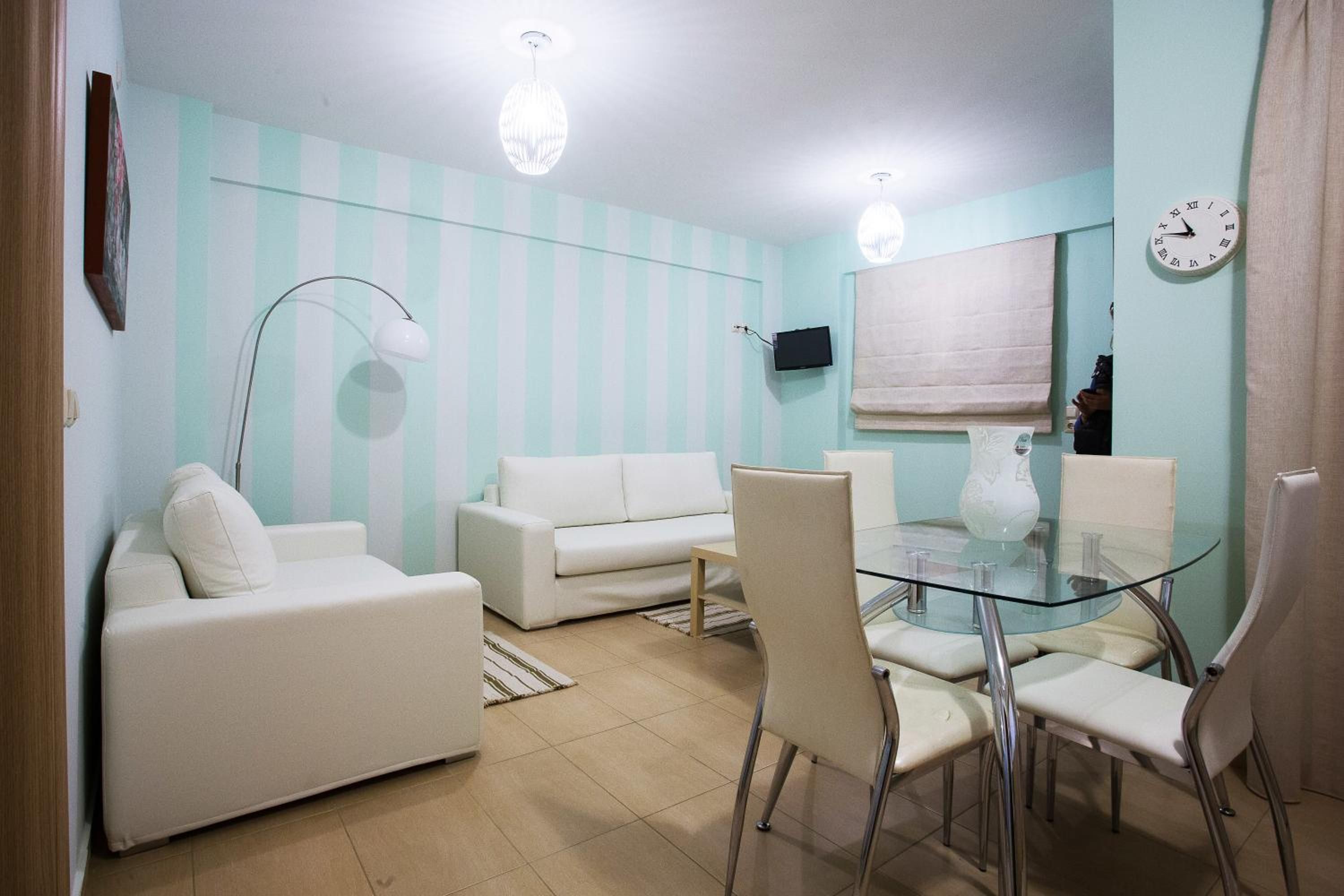 Sala de estar moderna com mesa de jantar de vidro, sofás brancos e TV na parede.