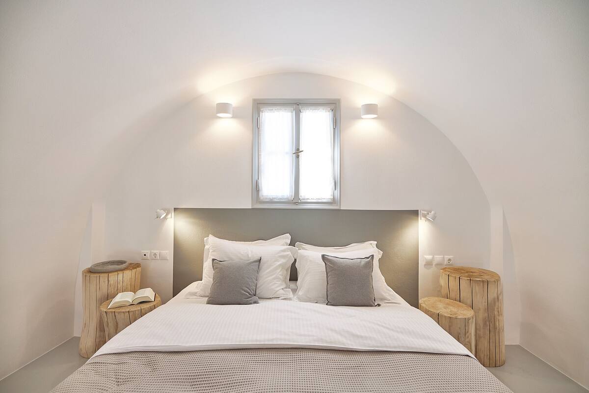 A bedroom with a bed, two bedside tables, a window, and a headboard.