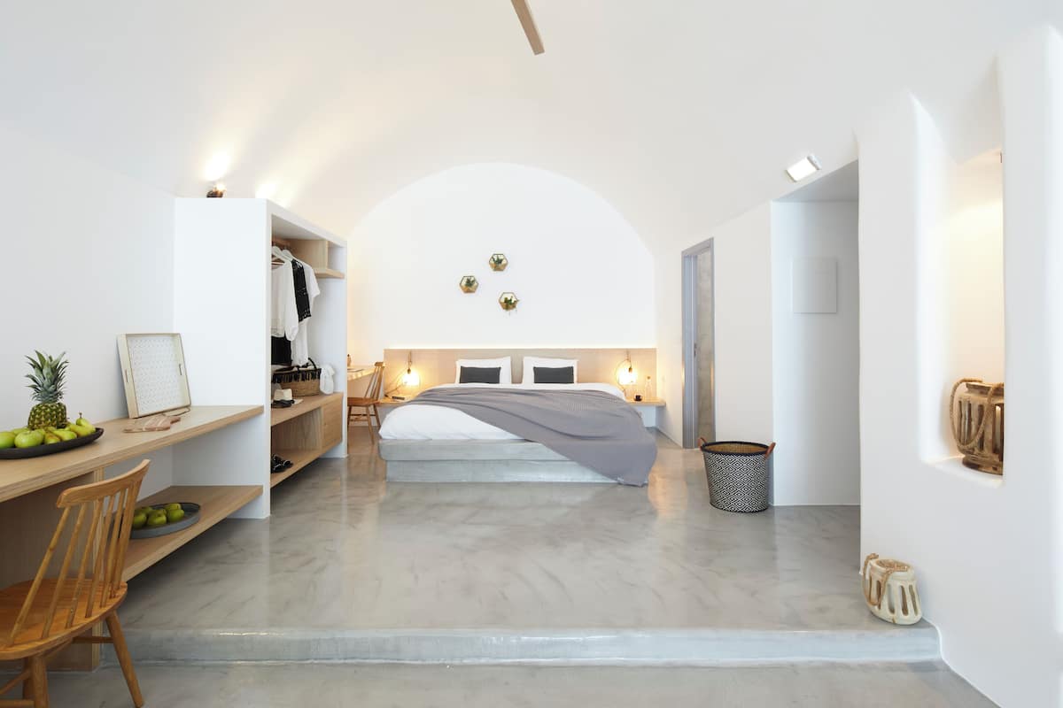 A modern bedroom with a bed centered in the room, a desk with a chair, a small dining table, and a fruit bowl.