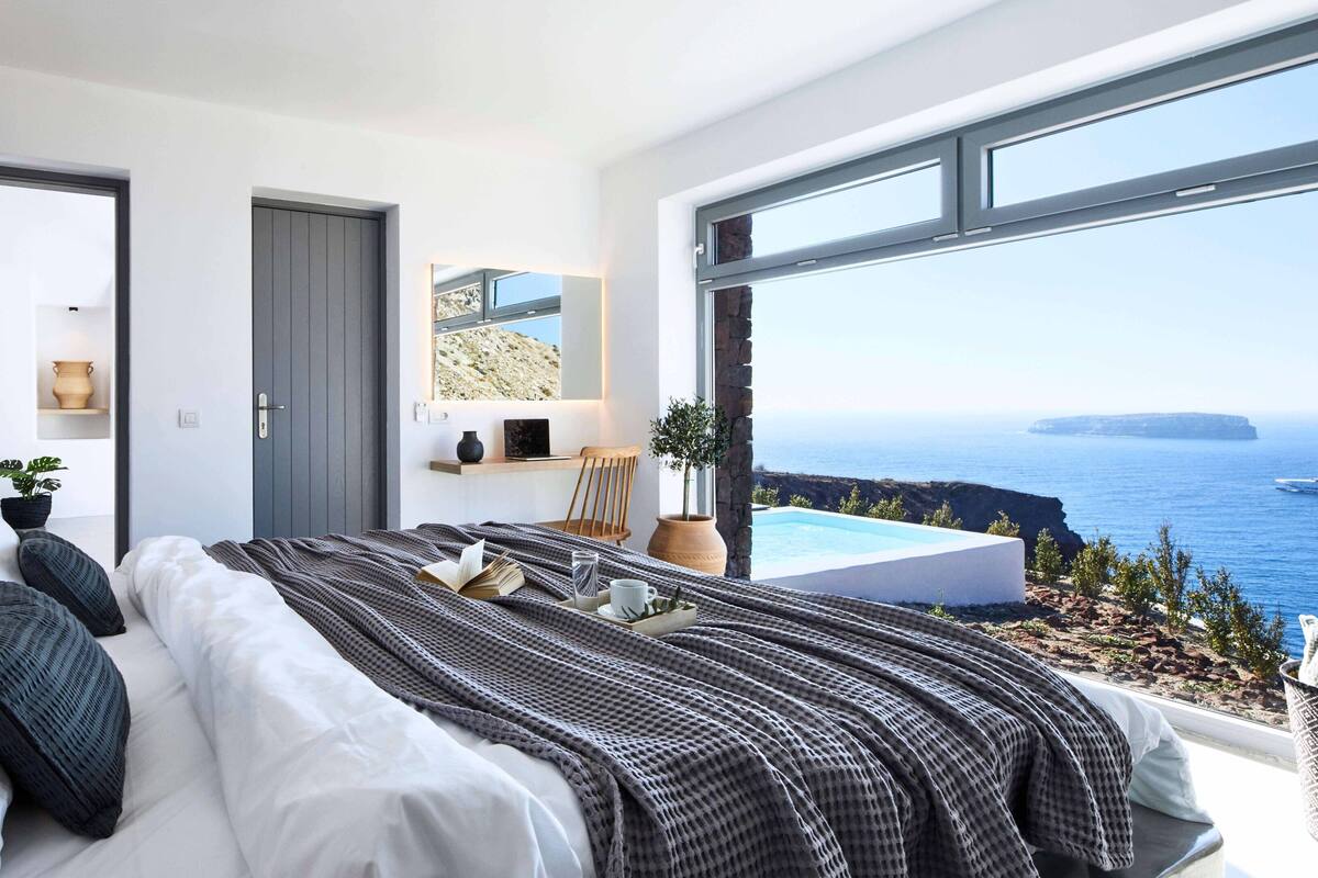 A modern bedroom with a large bed, a desk, and a view of the sea.