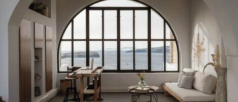 A cozy room with a large arched window, a wooden desk, a sofa, and a vase with dried plants.