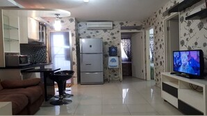 Un espacio habitable compacto con kitchenette, refrigerador, televisor y sofá.