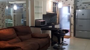 Un espacio habitable compacto con sofá, mesa de comedor y zona de cocina con refrigerador, y una pared con diseño.