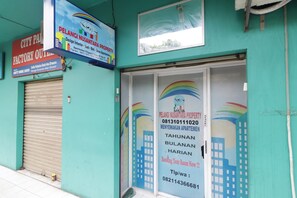 A building with a closed shutter door, a signboard for a property management company, and a contact number. - Apartment City Park by Nusantara Pelangi (Jakarta)