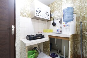 A compact kitchen with a gas stove, a water dispenser, and a large water bottle. - Apartment City Park by Nusantara Pelangi (Jakarta)