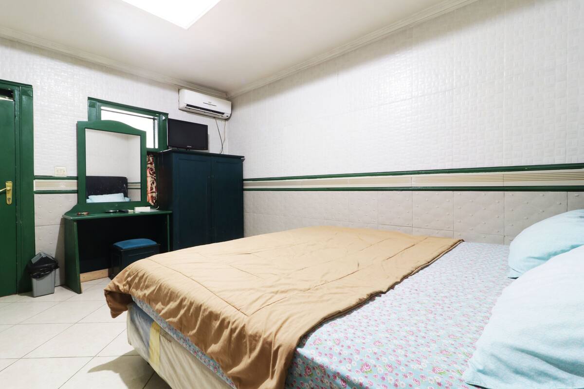 A bedroom with a bed, a desk, a mirror, and an air conditioning unit.