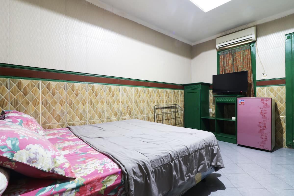 A bedroom with a bed, a television, a refrigerator, and an air conditioning unit.