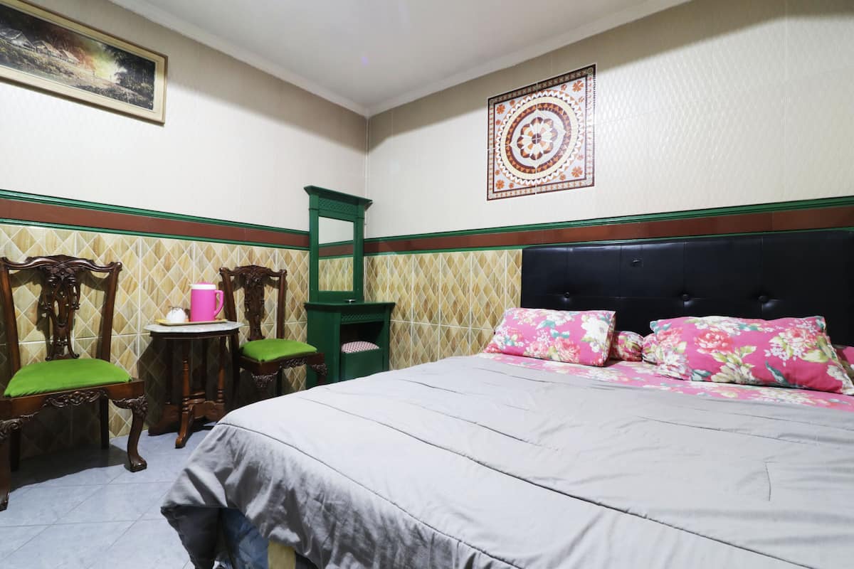A bedroom with a bed, two chairs with green cushions, a small table with a pink mug, and a green chair.