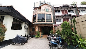 A two-story building with a balcony, a covered motorcycle, and several potted plants. - Hotel Alamanda (Jakarta)