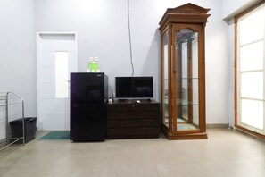 Una habitación con un refrigerador negro, un mueble de madera con puertas de cristal, un televisor sobre un aparador de madera, una estantería de metal y un cubo de basura.