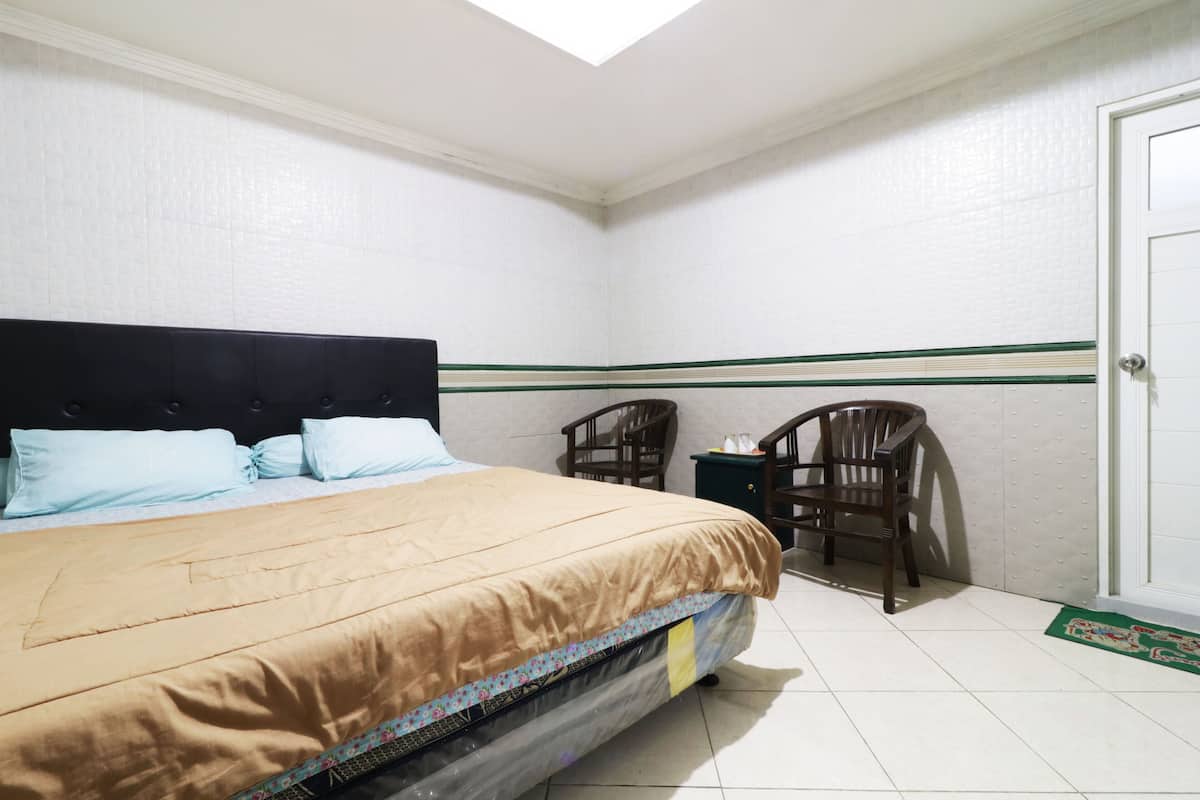 A bedroom with a bed, two chairs, a small table, and a door.