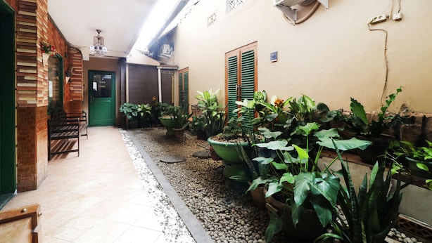 A narrow corridor with tiled flooring, green shutters, and potted plants. - Hotel Alamanda (Jakarta)