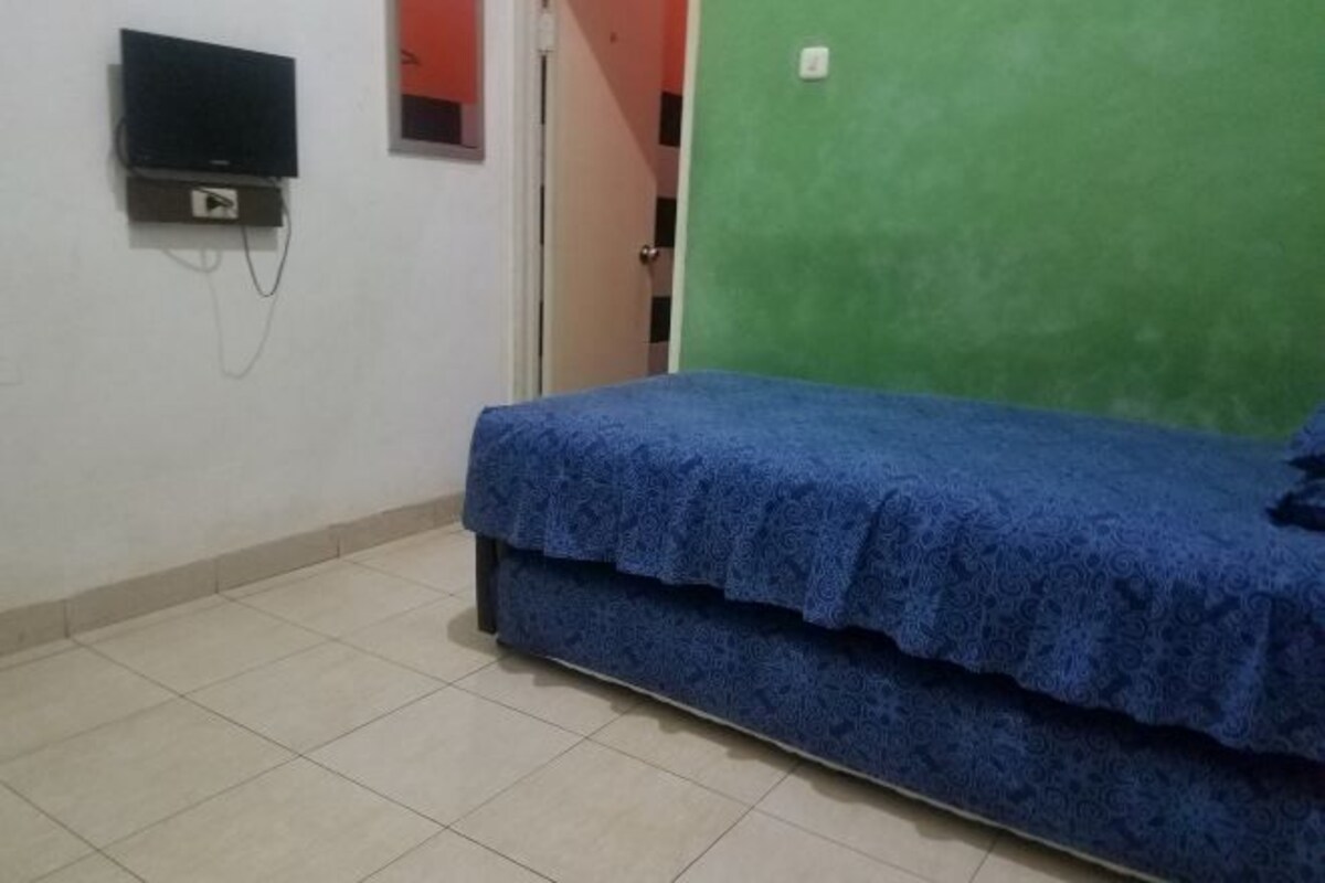 A room with a bed, a television mounted on the wall, and a green wall.