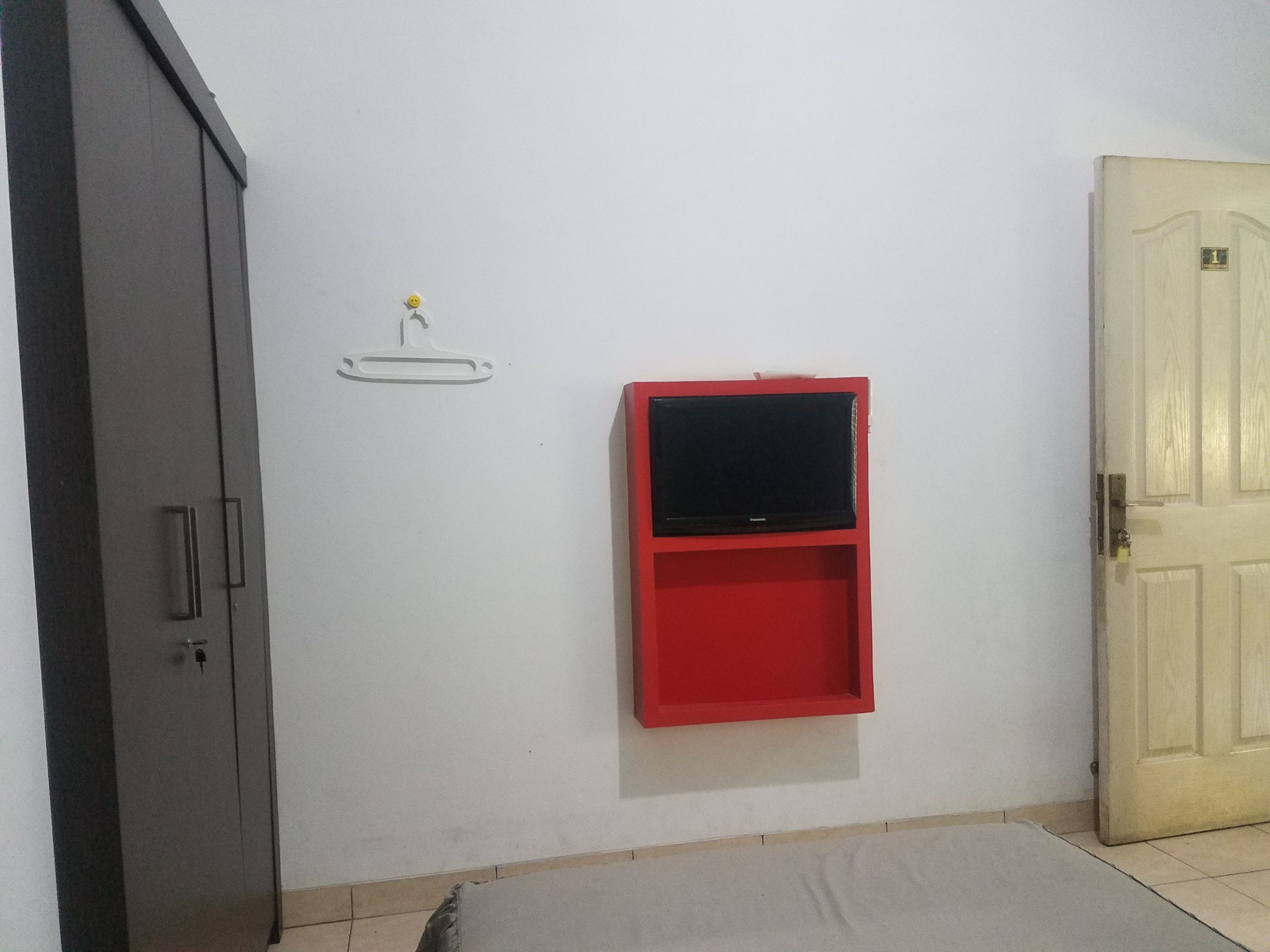 Een kamer met een gesloten deur, een rode tv-kast, een witte muur en een klein schap met een lamp.