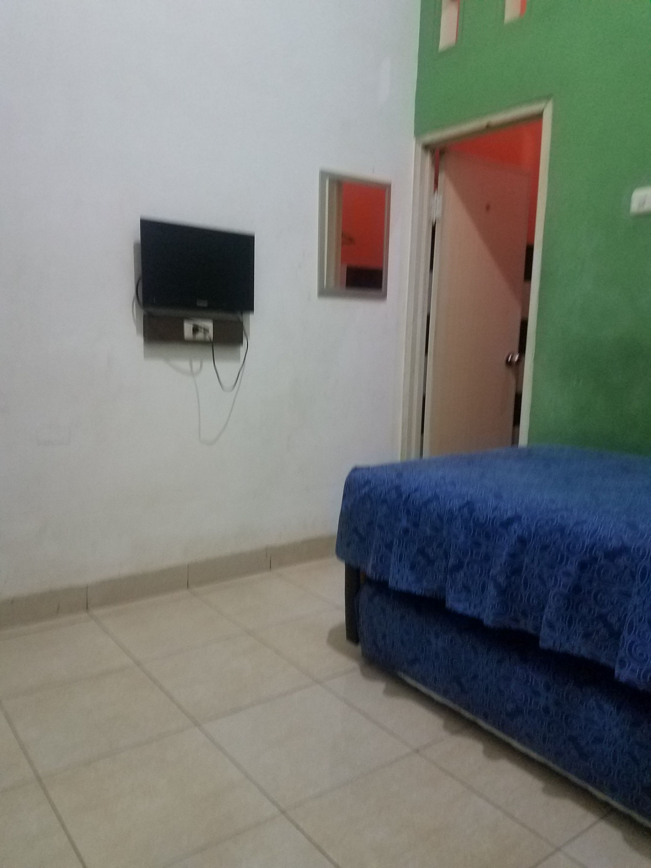A room with a bed, a television mounted on the wall, and a door.