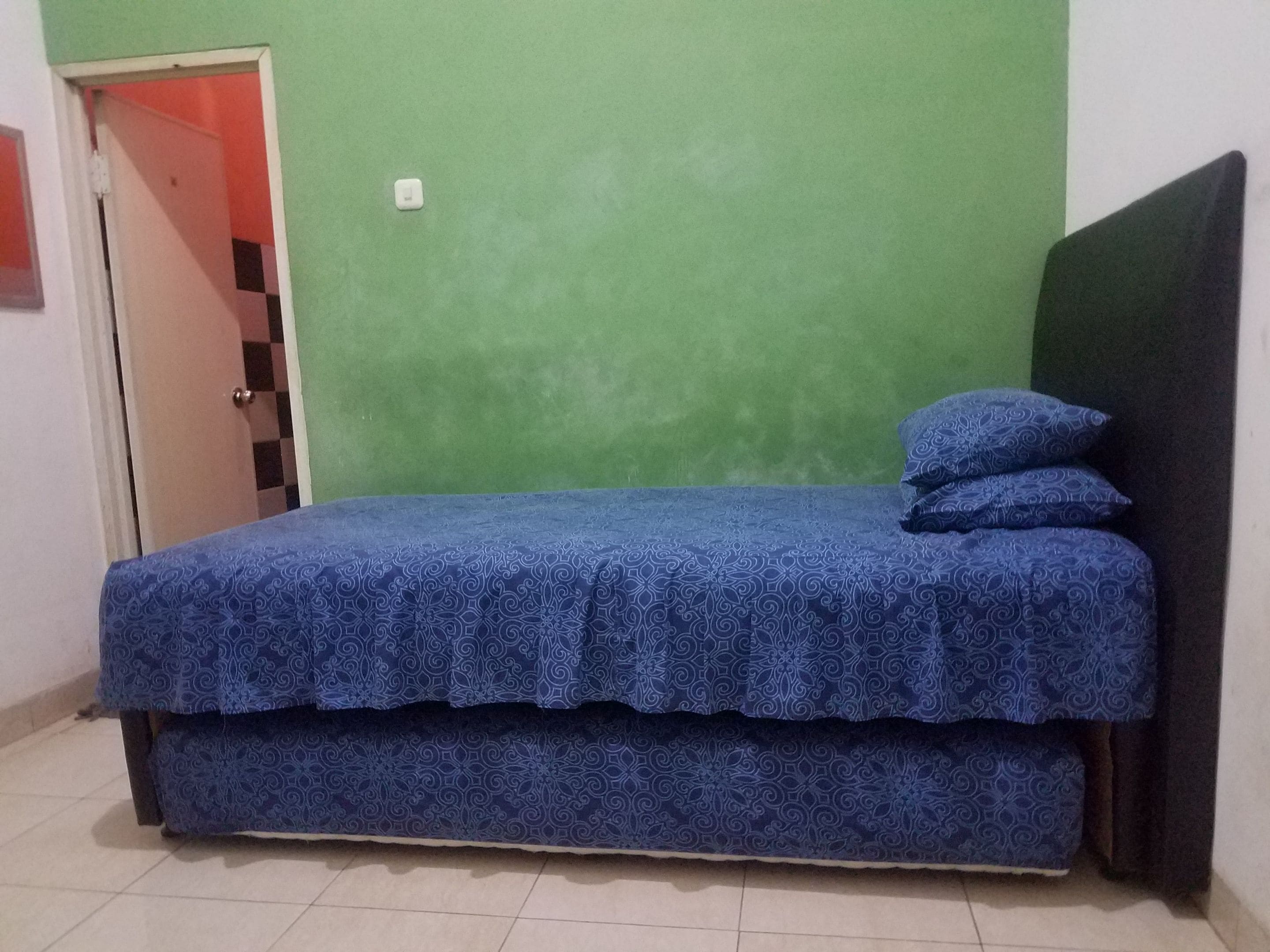 A small, single-bed room with a green wall and a black headboard.