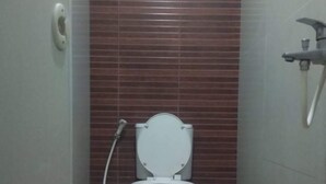 Un baño pequeño y cerrado con inodoro, secamanos y cabezal de ducha.