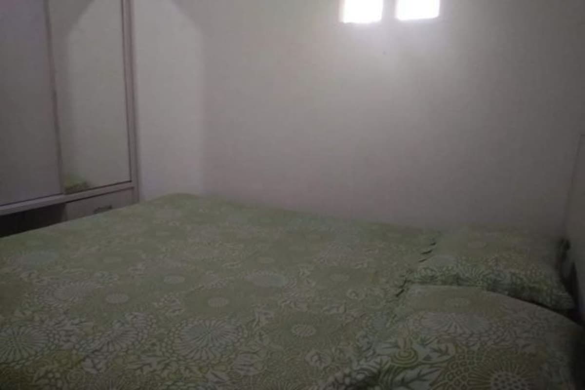 Ein Zimmer mit einem Bett, das mit einem gemusterten Überwurf bezogen ist, einem Kleiderschrank und einem kleinen Fenster, das für natürliches Licht sorgt.