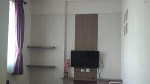 Una habitación con un televisor de pantalla plana montado en una pared de paneles de madera, un sofá morado y un mueble blanco pequeño.