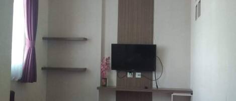 A room with a flat-screen TV mounted on a wooden panel wall, a purple sofa, and a small white cabinet.