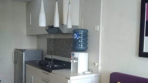 Cocina compacta con refrigerador, estufa y gabinetes blancos. Un sofá morado con cojines amarillos está en la sala.