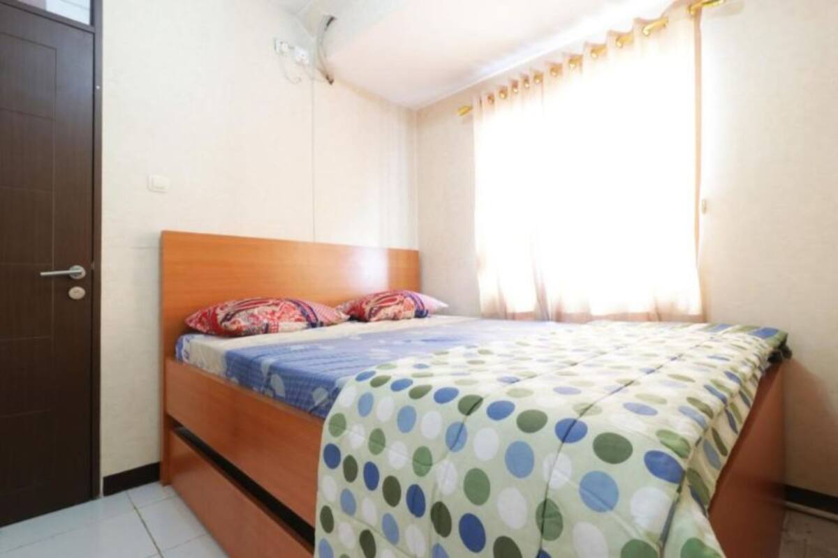 Un lit simple avec une tête de lit en bois, une couvre-lit à pois et une fenêtre avec des rideaux.