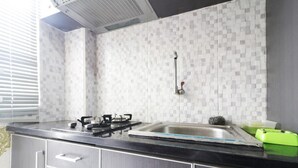 A kitchen with a gas stove, a sink, and a tiled backsplash. - Jo Rooms - Apartemen Betos (Bekasi)