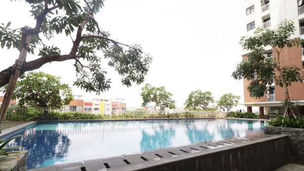 A swimming pool surrounded by trees and a multi-story building. - Jo Rooms - Apartemen Betos (Bekasi)