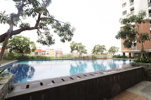 Une piscine entourée d’arbres et un immeuble à plusieurs étages.