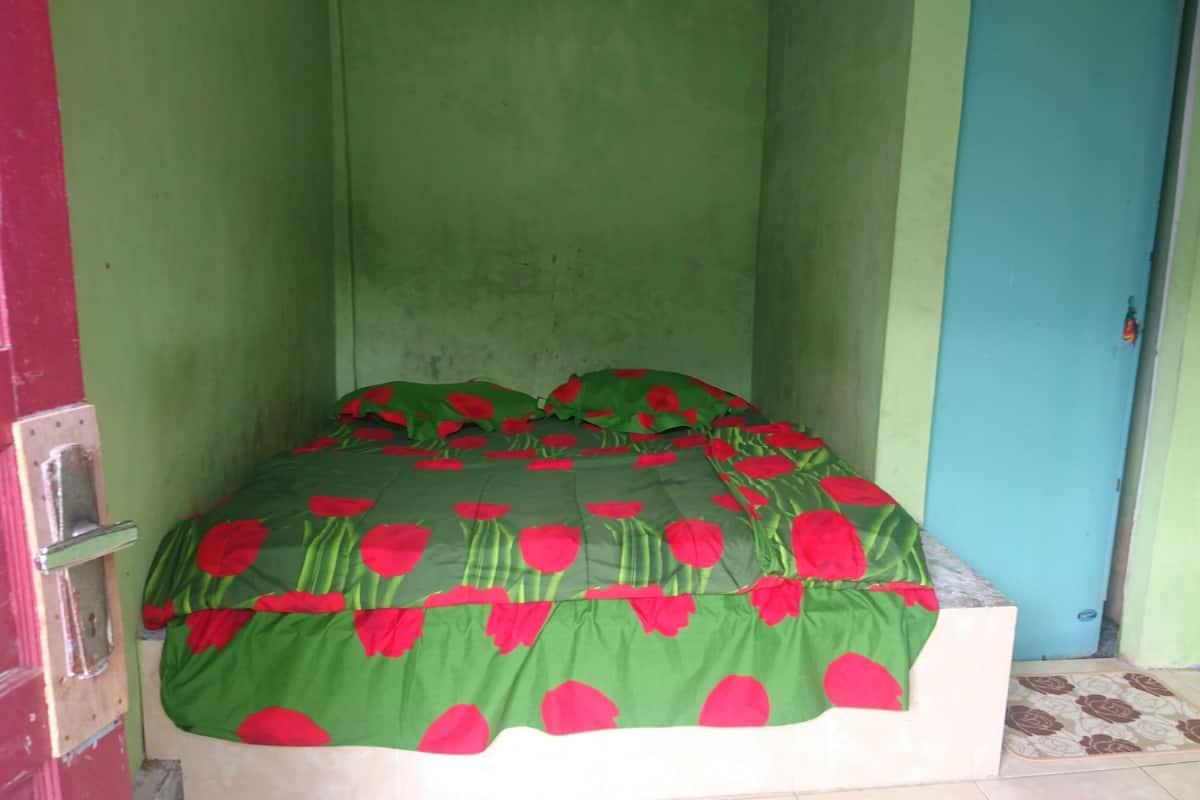 Una habitación pequeña y estrecha con una cama individual, paredes verdes y una puerta azul.