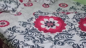 A bed with a patterned bedspread featuring floral designs in red, black, and white. - Penginapan Biringta (Berastagi)