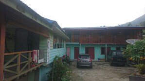 A two-story building with a satellite dish, a car parked in front, and a dirt driveway. - Penginapan Biringta (Berastagi)