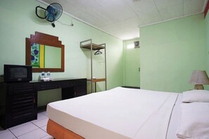 A room with a bed, a desk with a television, a mirror, a fan, and a lamp. - Hotel Bandung Permai (Bandung)
