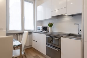 A modern kitchen with white cabinets, stainless steel appliances, and a window providing natural light.
