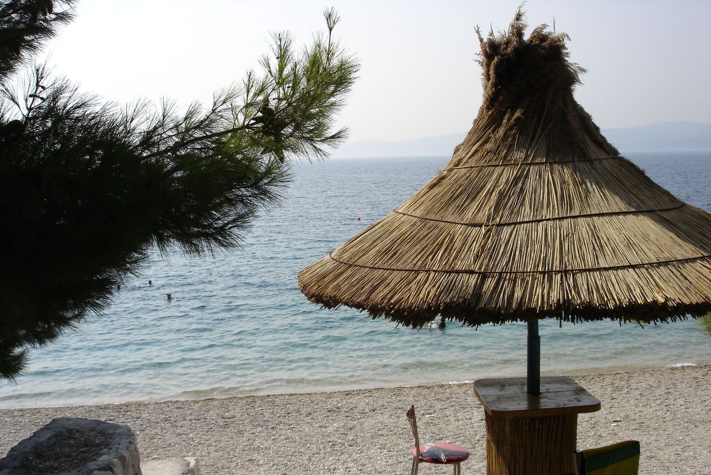 A beach scene with a thatched umbrella, a rocky shoreline, and the sea in the background.