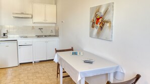 Una cocina con armarios blancos, una mesa blanca con mantel y un cuadro en la pared.